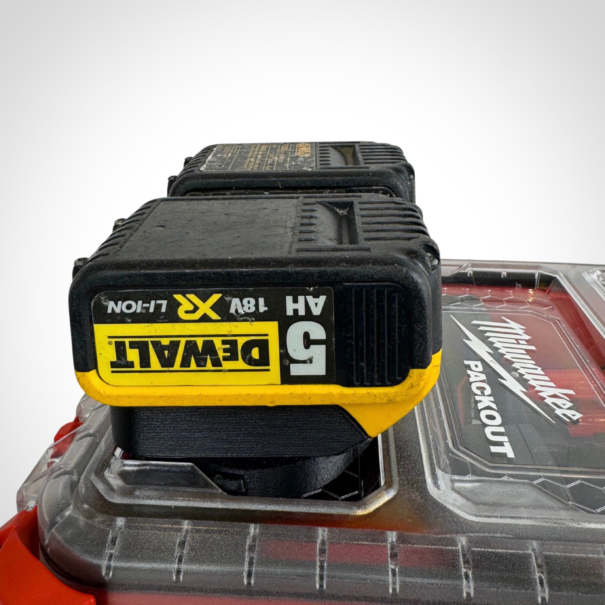 DeWalt 18V batteries securely seated in the adaptor insert ontop a Milwaukee PACKOUT™ Compact Organiser, ready for transport.