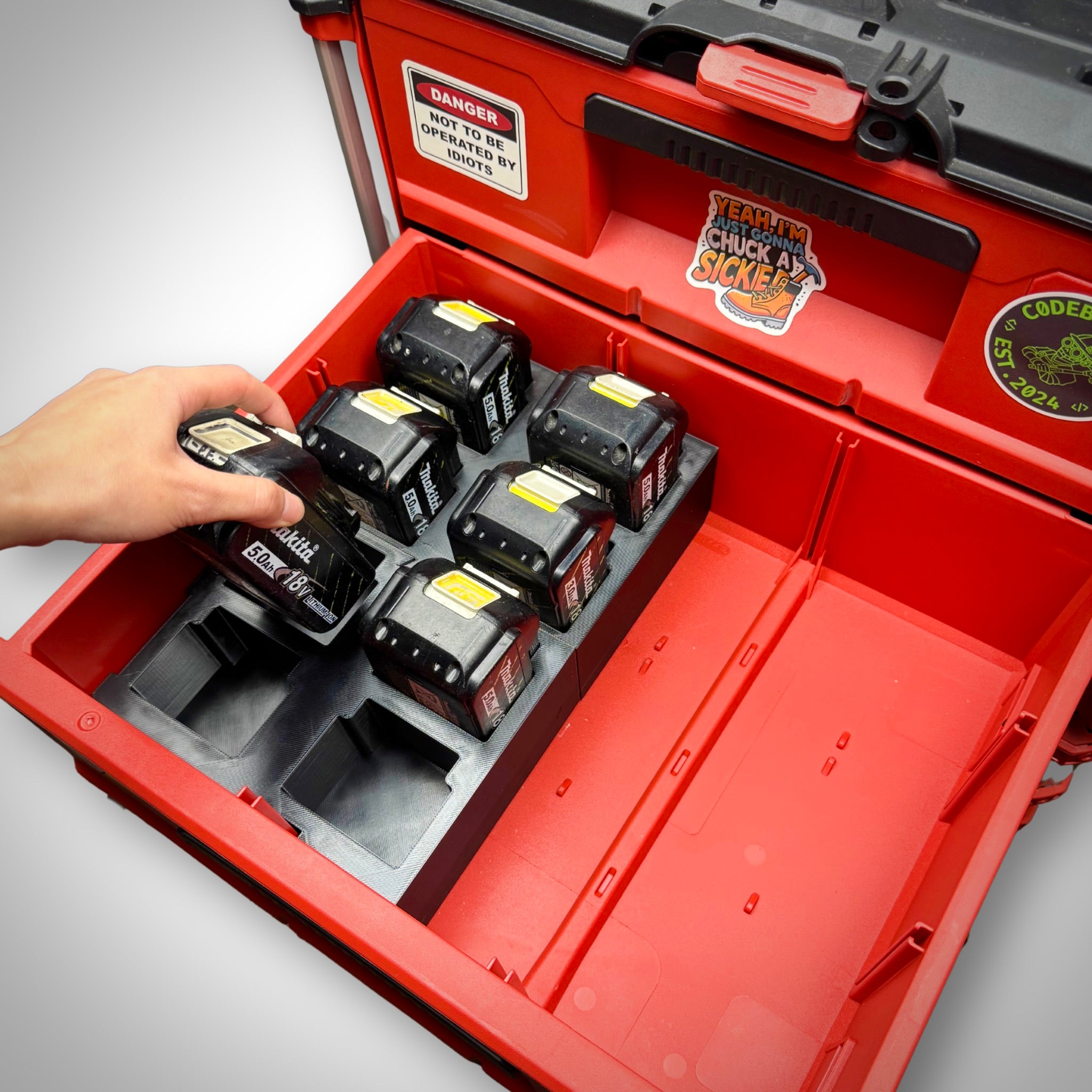 Hand removing a Makita 18V battery from the storage insert inside the Milwaukee PACKOUT™ Two-Drawer Toolbox, demonstrating quick and easy access.