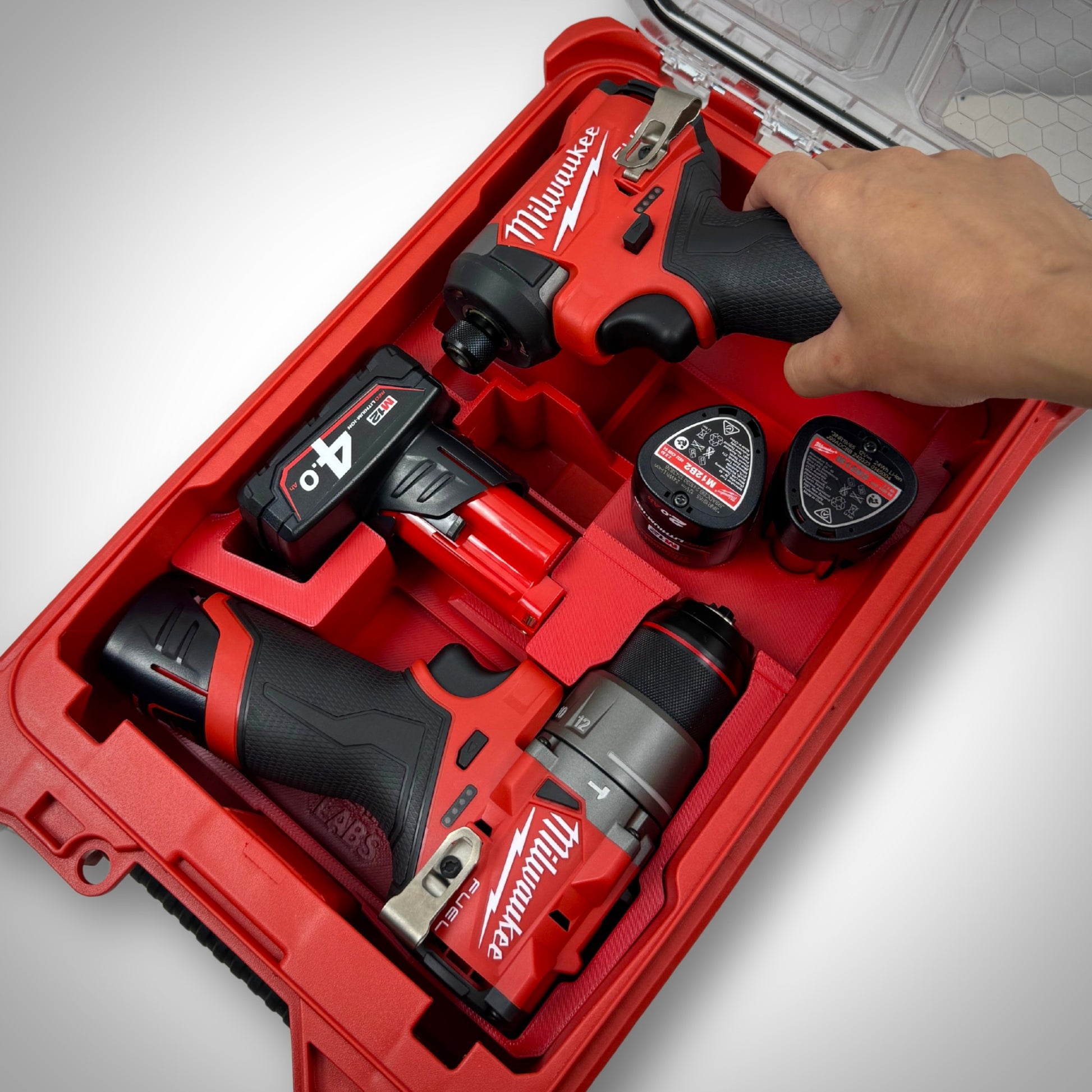 Hand lifting the M12 Impact Driver from the red insert, while other components remain securely organised in the PACKOUT™