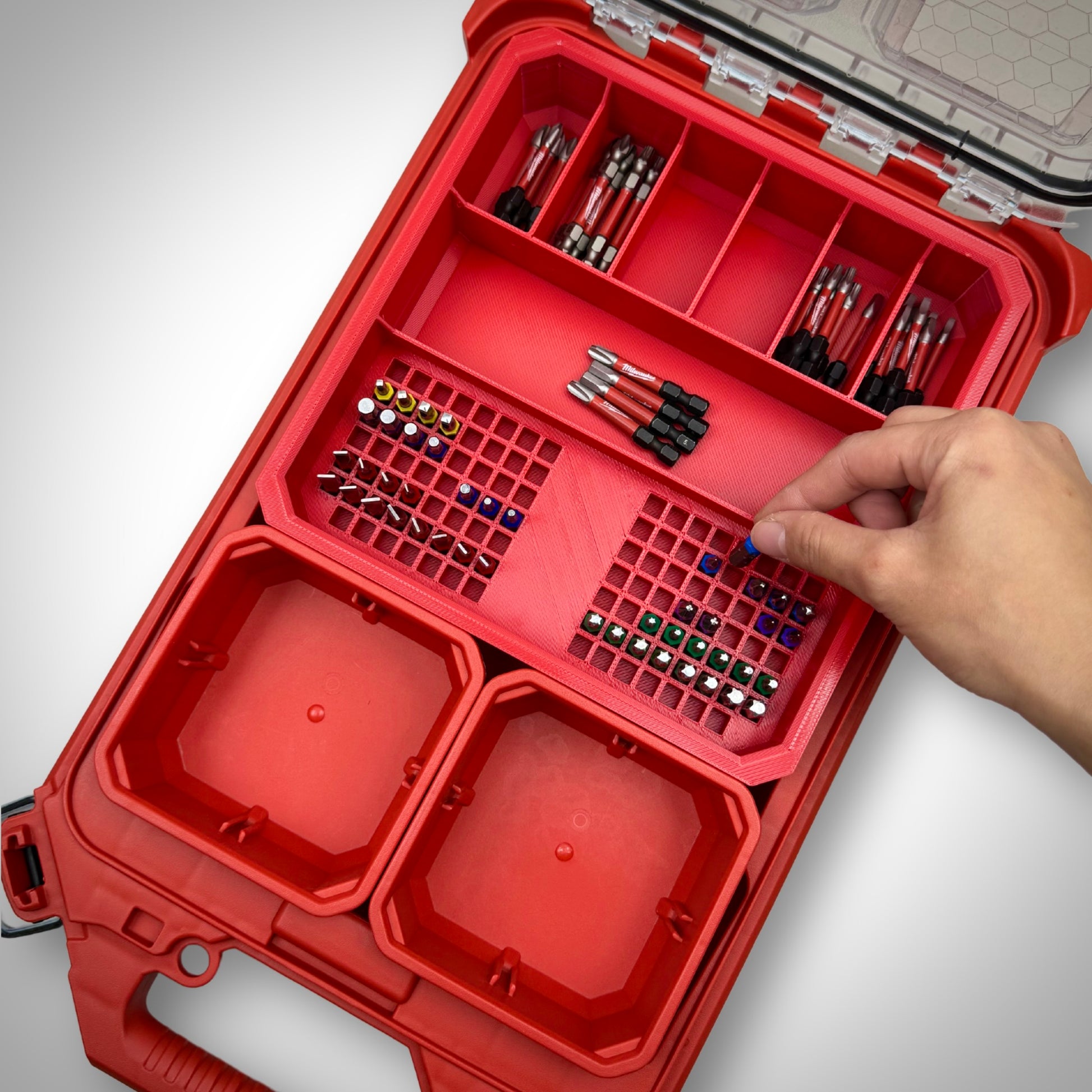 Hand picking a 50mm impact bit from the loaded red Impact Bit Holder V2 inside the Milwaukee PACKOUT™ Low Profile Organiser, demonstrating quick and easy access.