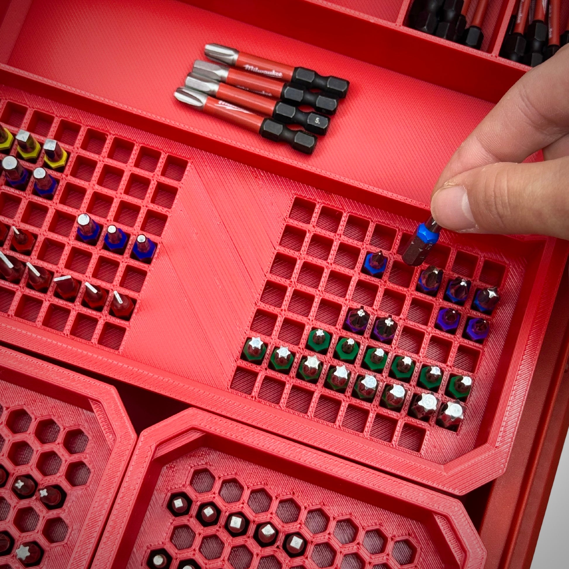 Hand reaching into a Milwaukee PACKOUT™ Low Profile Organiser to retrieve a bit from the red Bit Organiser Combo insert, highlighting easy and efficient access.