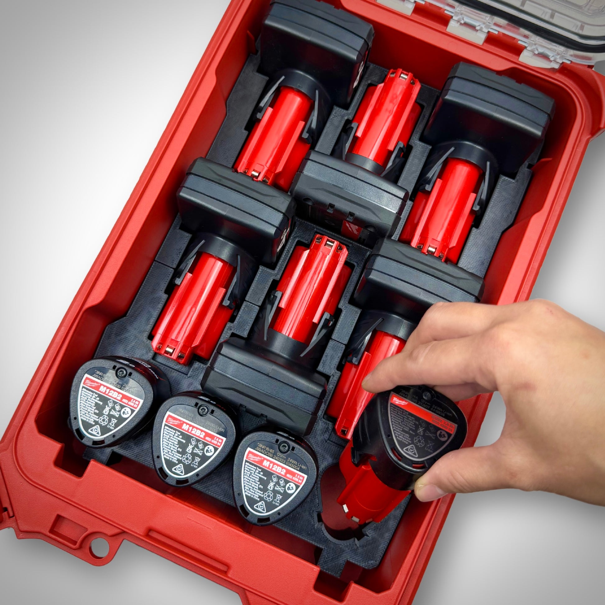 Hand picking an M12 battery from the fully loaded black M12 Battery Storage Insert inside the Milwaukee PACKOUT™ Compact Organiser, showing easy and quick battery access.