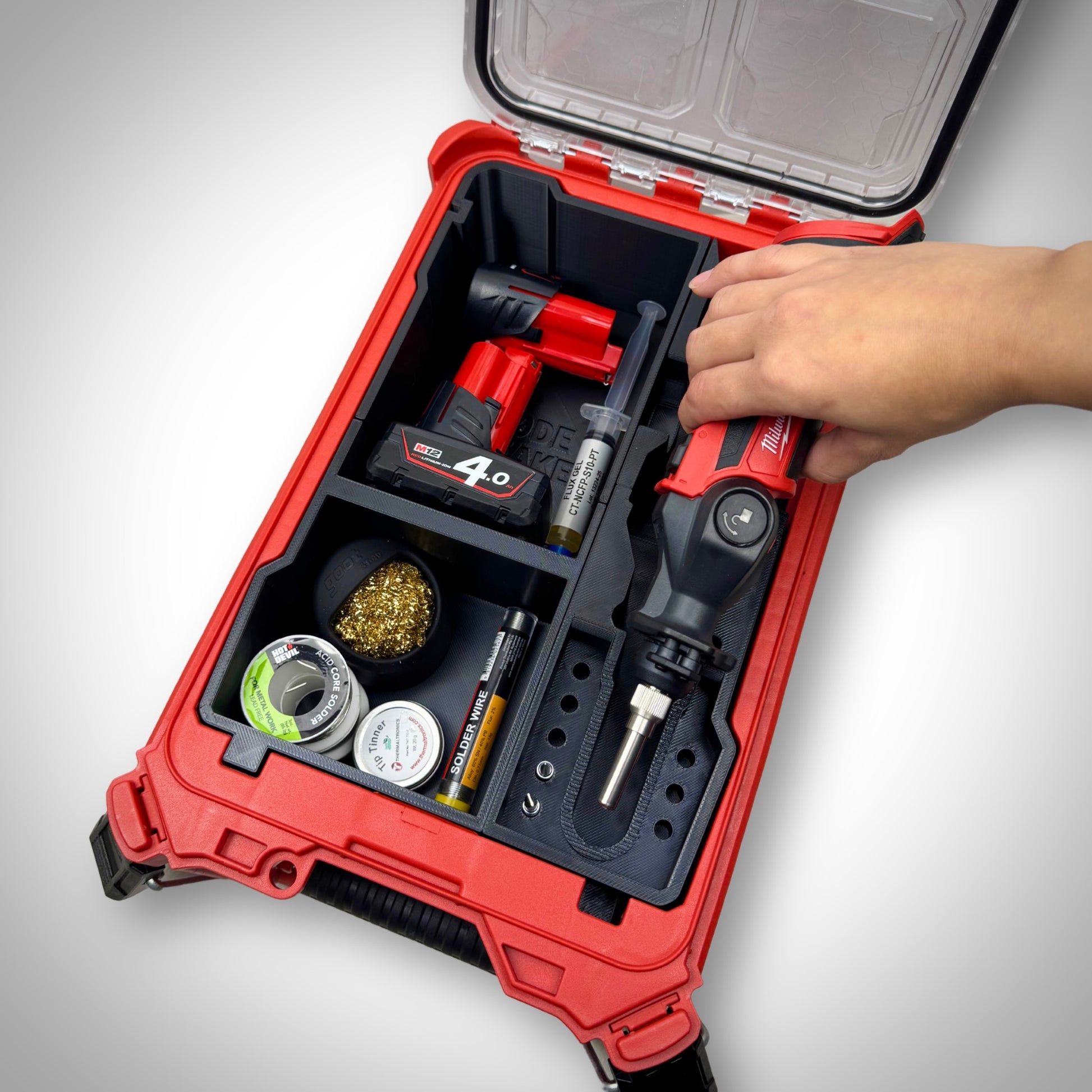 Hand lifting the Milwaukee M12 soldering iron from the loaded M12 Soldering Iron Insert inside the PACKOUT™ Compact Organiser, showing quick and easy access on-site.