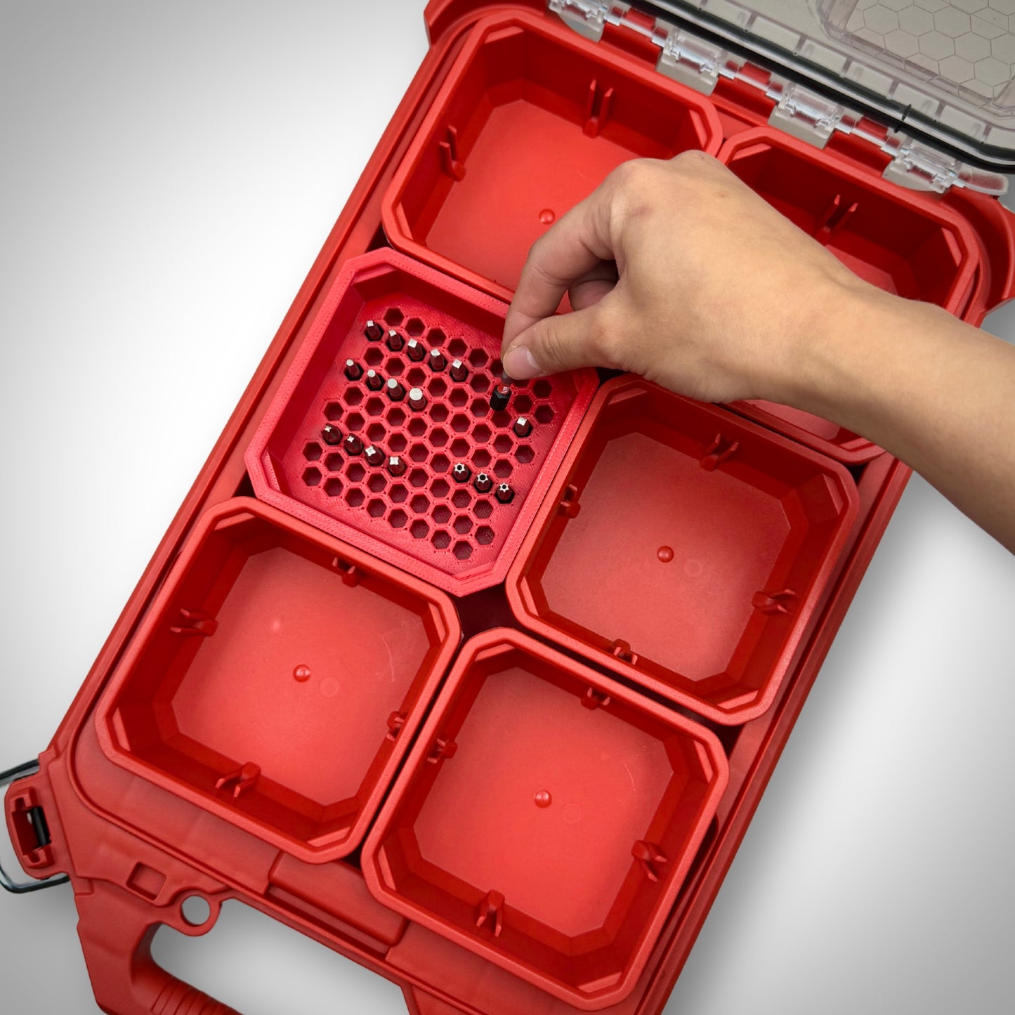 Hand removing a hex bit from the red Hex Bit Holder insert inside a Milwaukee PACKOUT™ bin, demonstrating easy access and tidy storage.
