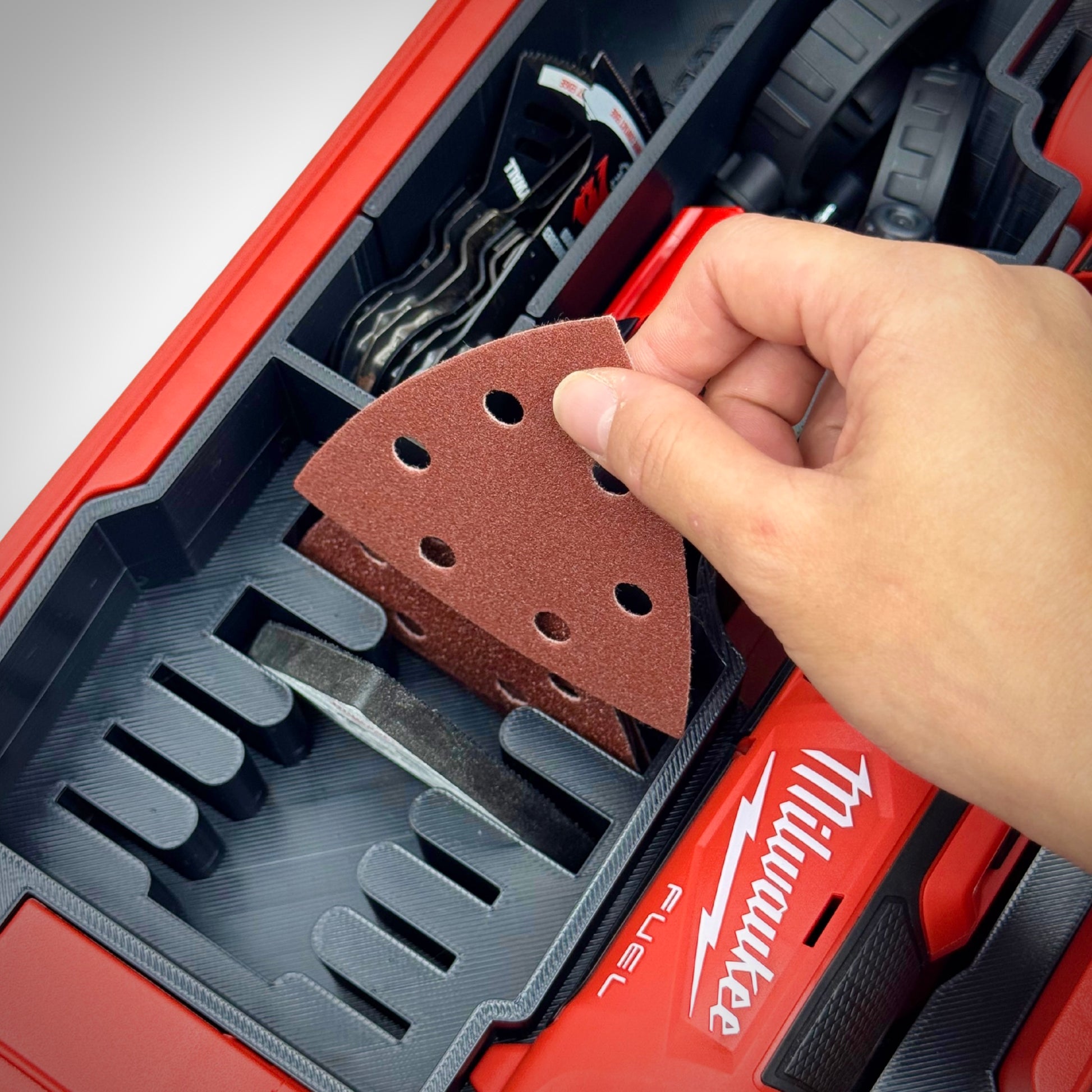 Hand lifting a M12 FUEL Multi-Tool accessory from the insert inside the PACKOUT™ Compact Organiser, demonstrating quick and easy access.