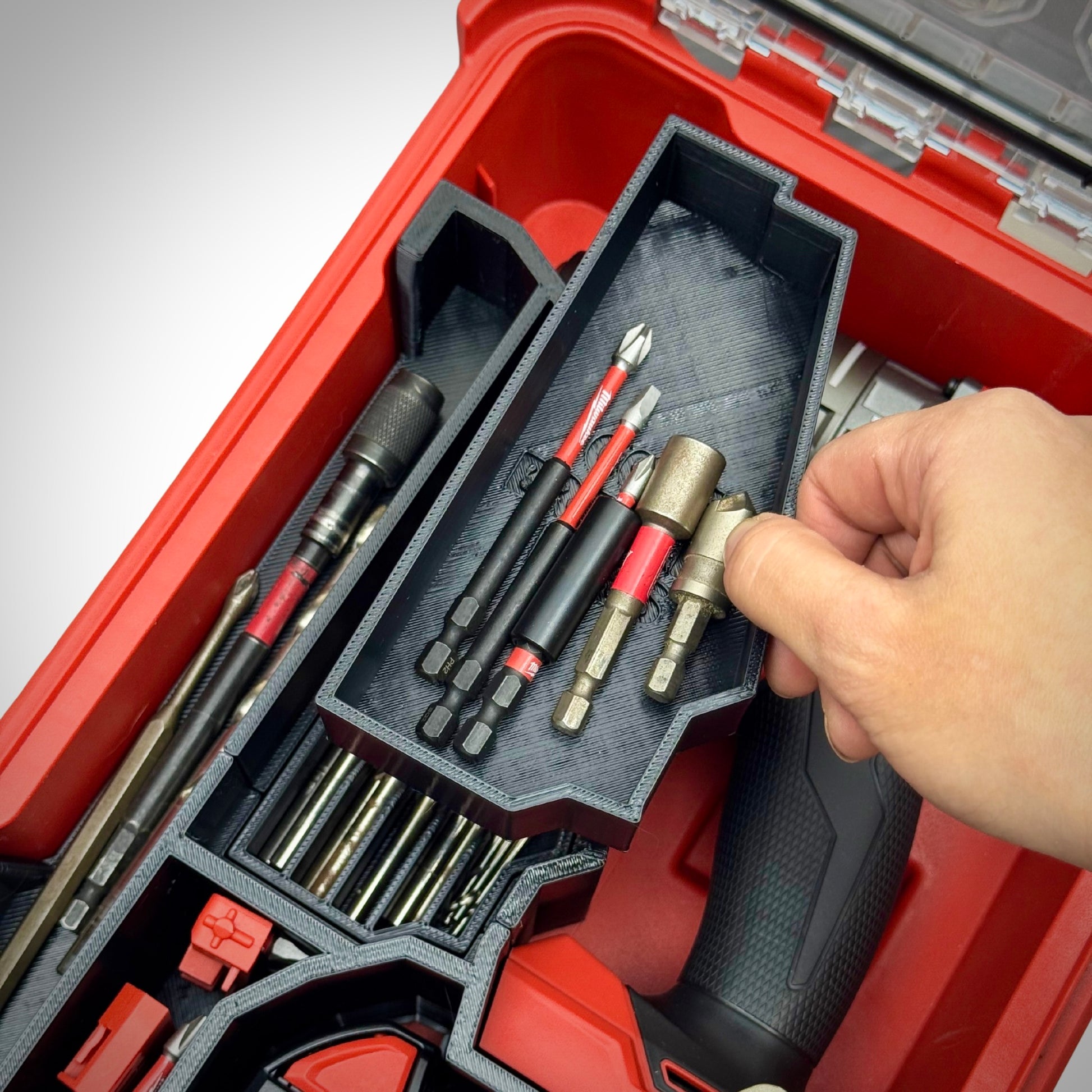 Hand removing a tray from the M18 Drill Insert inside the PACKOUT™ Compact Organiser, revealing hidden storage space below.