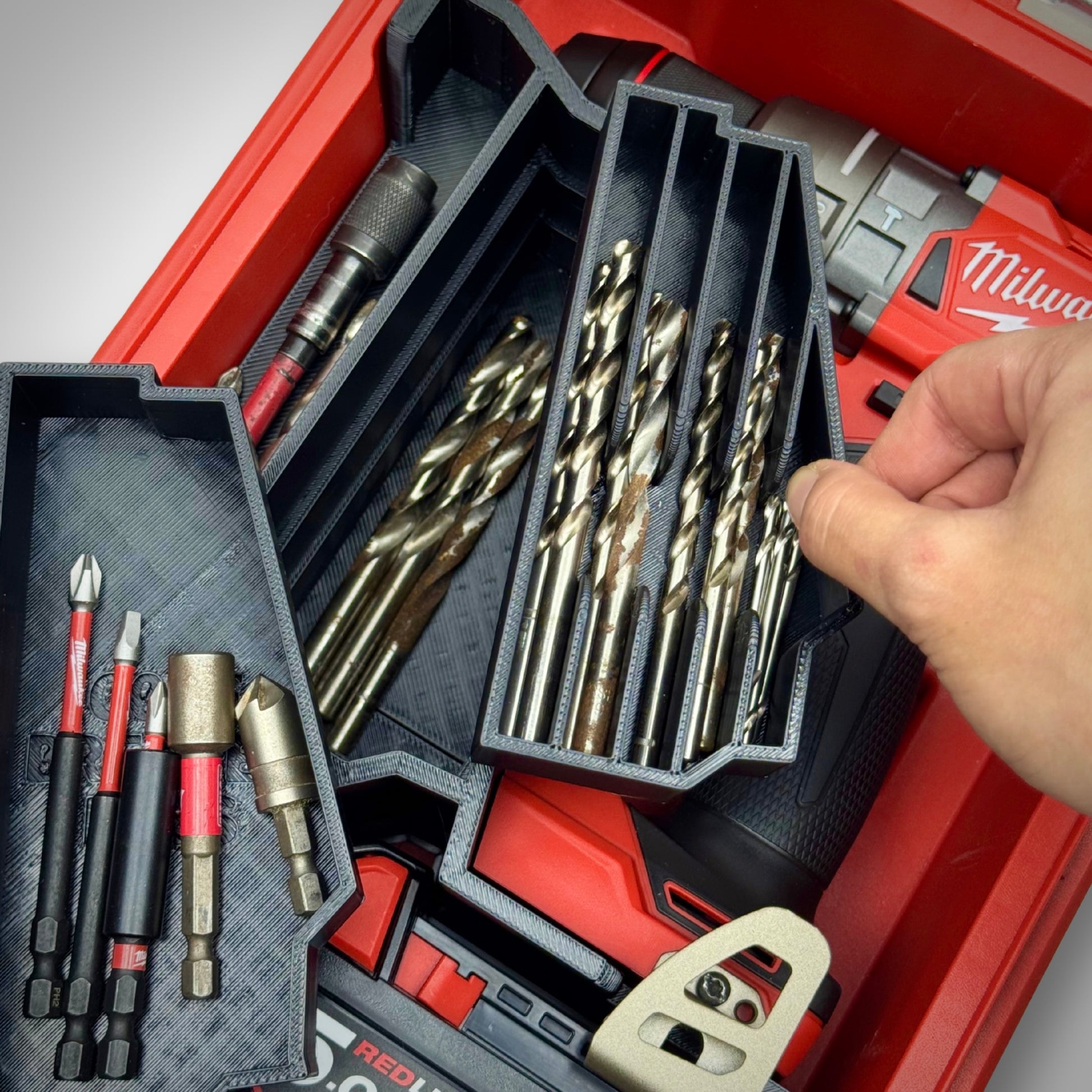 Hand removing two of the trays from the M18 Drill Insert inside the PACKOUT™ Compact Organiser, revealing hidden storage space below.